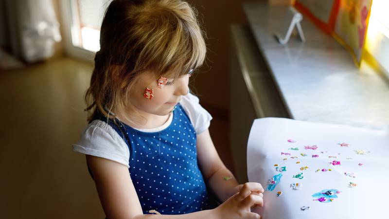 Little toddler girl playing with different colorful animal sticker. Happy funny child having fun with stick stickers on face